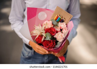 Boy dressed in a white shirt holding a festive bouquet decorated with a box of colorful pencils - Shutterstock ID 1144221701