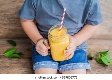 Boy Drinking Juicy Smoothie From Mango In Glass Mason Jar With Striped Red Straw On Old Wooden Background. Healthy Life Concept, Copy Space.