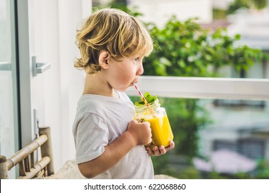 Boy Drinking Juicy Smoothie From Mango In Glass Mason Jar With Striped Red Straw On Old Wooden Background. Healthy Life Concept, Copy Space.