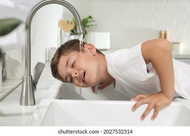 Boy Drinking Tap Water Over Sink In Kitchen