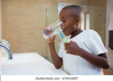 Boy Drinking Water From Glass While Standing By Sink