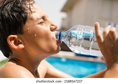 Boy drinking water from a plastic bottle under a scorching sun. Heat wave. Child drinking bottled water due to high temperatures in summer. Child in pool drinking water to withstand heat wave. - Powered by Shutterstock