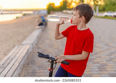 A boy drinks water from plastic bottle, standing with scooter - Powered by Shutterstock