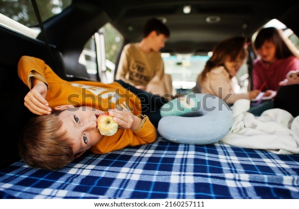 Boy eat apple. Mother with four kids at vehicle\
interior. Children in trunk. Traveling by car, lying and having\
fun, atmosphere concept.