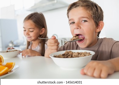 Boy Eating Cereal While Having Breakfast With His Sister In The Kitchen