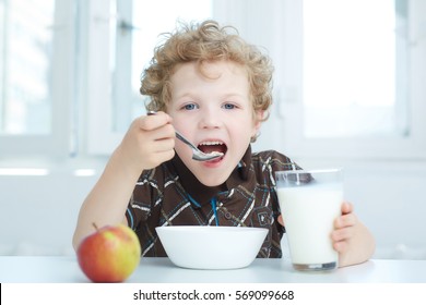 Boy Eating Cereal While Having Breakfast  In The Kitchen.