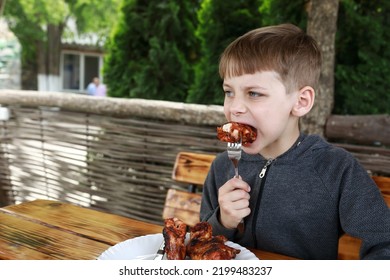 Boy Eating Grilled Chicken Wings On Restaurant Terrace