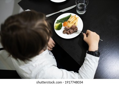 Boy Eating A Healthy Meal Of Steak And Vegetables At The Dinner Table.