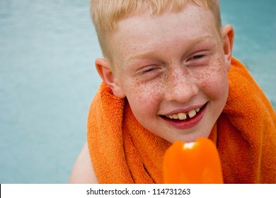 Boy eating orange popsicle by a swimming pool