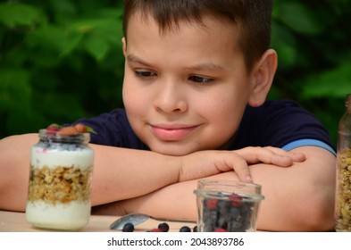 Boy Eating Wholesome Healthy Breakfast, Yogurt, Muesli And Fresh Berries From A Jar Outdoors, In A Garden Or Cafe. Happy Family Having Breakfast.