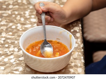 Boy eats soup with a spoon from a white plate.