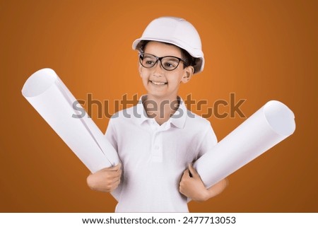 a boy engineer in a hard hat and glasses with blueprints on a blue background. studio photo.