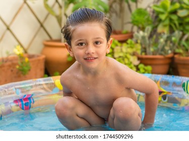 Boy Enjoying Summer In The Pool At Home. Boy Playing In The Kiddie Pool In The Backyard. Summer At Home Concept