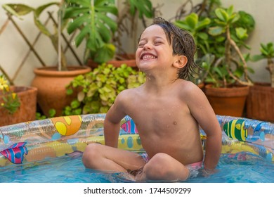 Boy Enjoying Summer In The Pool At Home. Boy Playing In The Kiddie Pool In The Backyard. Summer At Home Concept