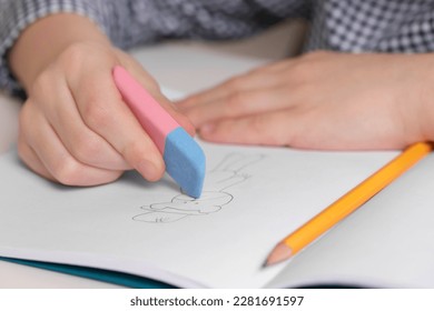 Boy erasing mistake in his notebook at white desk, closeup