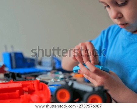 Boy Examining Small Plastic Component at Cluttered Toy Workbench — Child Tinkering and Building, Hands-On Play, STEM Curiosity and Engineering Mindset Concept