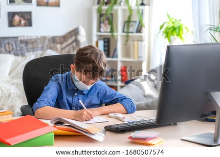 Boy in face mask with computer does his homework during a coronavirus quarantine. concept of online education. Social distance, self- isolation. Distance learning due to virus, flu, epidemic COVID-19