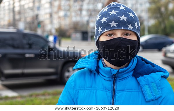 boy in face mask on street near road with\
cars. Child walks during quarantine and lockdown. child protected\
from viruses, pollution in bad epidemic situation, among patients\
with coronavirus