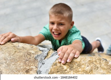 boy falls from the mountain and holds fingers over edge of wall. child is in danger. Active extreme outdoor games. The child is hanging on a stone wall. - Powered by Shutterstock