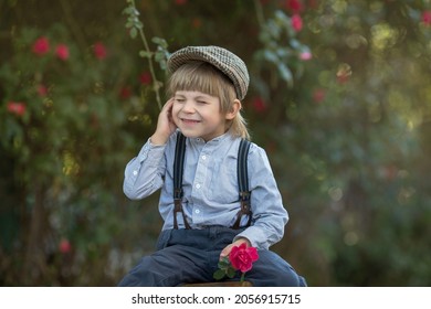 A Boy In Fashionable Vintage Clothes Is Sitting In The Garden With A Rose In His Hand And Holding His Cheek And Ear With His Hand. The Concept Of Insect Bite, Itchy Skin.