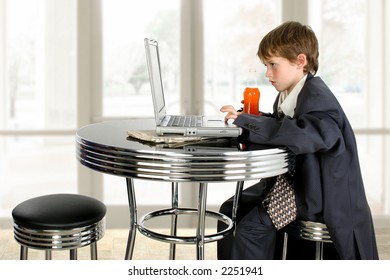 Boy in father's suit at table with soda and laptop.