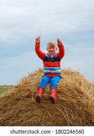 boy in the field playing on a stack of straw