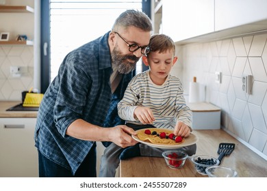 Boy filling pancake with fruit, sweets. Father spending time with son at home, making snack together, cooking. Fathers day concept. - Powered by Shutterstock