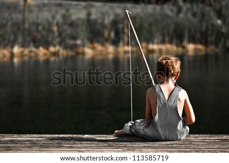 Boy fishing in overalls from a dock on a lake or pond with text space to the left.