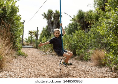 The boy is flying on a zip line in the park. A child is happily rocking on a zip line on a sunny playground. - Powered by Shutterstock