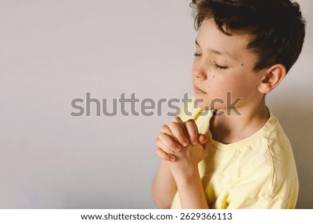 A boy with folded hands in front of him, he is praying or meditating. Concept of Christianity, religion and faith.