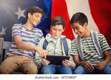 Boy with friends using digital tablet on bench against crumbled american flag 