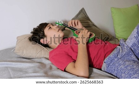 The boy gazes thoughtfully while lying down, embracing a moment of calm with his toy guitar.