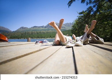 Boy And Girl (7-10) Lying Side By Side On Lake Jetty, Shoes Off, Rear View (surface Level)