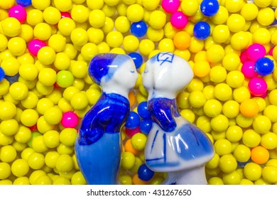 Boy And Girl Ceramic Doll Kissing With Plastic Balls Bearing Background