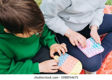 Boy And Girl Children Playing Colorful Poppit Sensory Game. Close Up Of Kid Hands Pushing Multi Colorful Trendy Pop It Bubble Flexible Fidget Toy. Anxiety Relif, Antistress, Mental Health Concept.