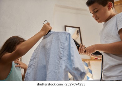 A boy and girl collaborate on ironing a shirt in a sunlit room, showcasing teamwork and responsibility. - Powered by Shutterstock