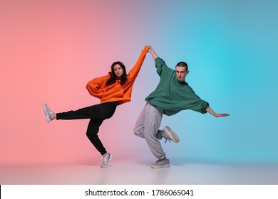 Anak laki-laki dan perempuan menari hip-hop dalam pakaian bergaya pada latar belakang gradien warna-warni di aula dansa di neon. Budaya pemuda, gerakan, gaya dan mode, tindakan. Potret cerah yang modis. Tari jalanan.