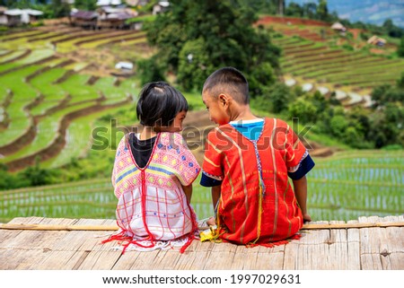 A boy and a girl dressed in hill tribe clothing are sitting on the terraced rice fields. 
