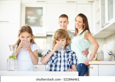 Boy and girl drinking water with lime in the kitchen while the parents are watching