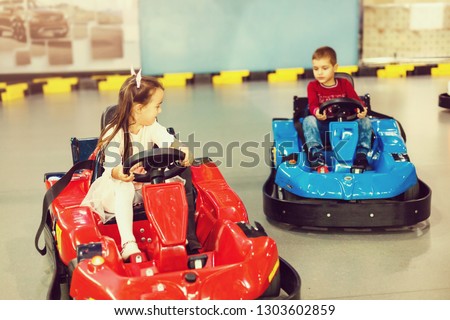 Boy and girl driving race bumper cars in autodrom indoors