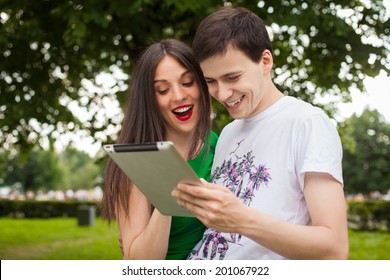boy and girl in green dress holding ipad together outdoor in the park 