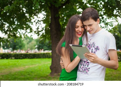 Boy And Girl In Green Dress Holding Ipad Together Outdoor In The Park 