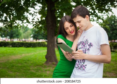 Boy And Girl In Green Dress Holding Ipad Together Outdoor In The Park 