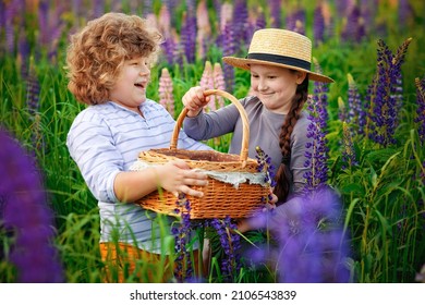 A boy and a girl in a hat holding a basket, standing in a field with tall blue-purple flowers, a summer landscape. Children in the field of lupins.