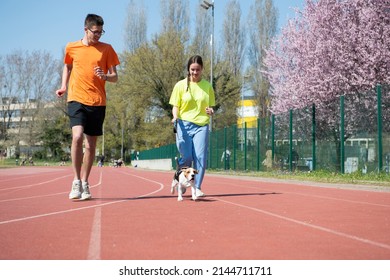 A boy, a girl and her beagle dog are running on the athletic track