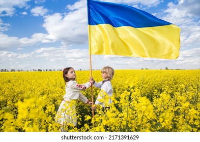 boy and girl hold yellow-blue flag, stand among flowering yellow rapeseed field. independence Day. Children of Ukraine for Peace. Support and help Ukraine. Be proud that you are Ukrainian.