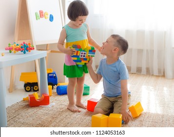 A boy and a girl are holding a heart made of plastic blocks. Brother and sister have fun playing together in the room. Preschool children and educational toys
