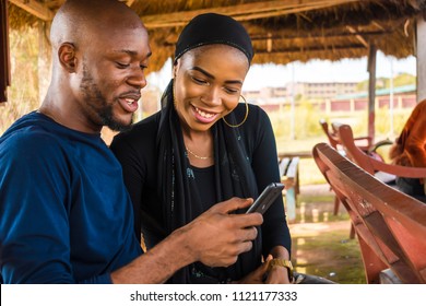 boy and a girl looking at something on a mobile phone. two people viewing something interesting on a phone, girl is smiling with her hair covered