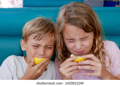Boy and girl making faces as they bite into lemons