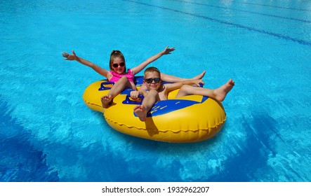 Boy And Girl On Inflatable Float In Outdoor Swimming Pool. Summer Water Play Kids. Little Children Floating On Yellow Raft In Aquapark.